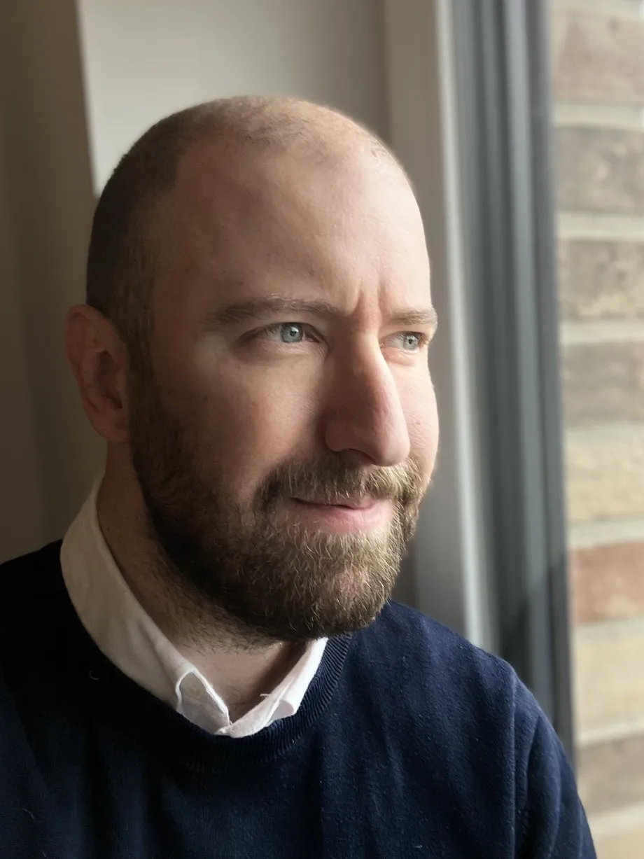Tobias Friedl am Fenster, lächelnd, den Blick nach draußen gerichtet